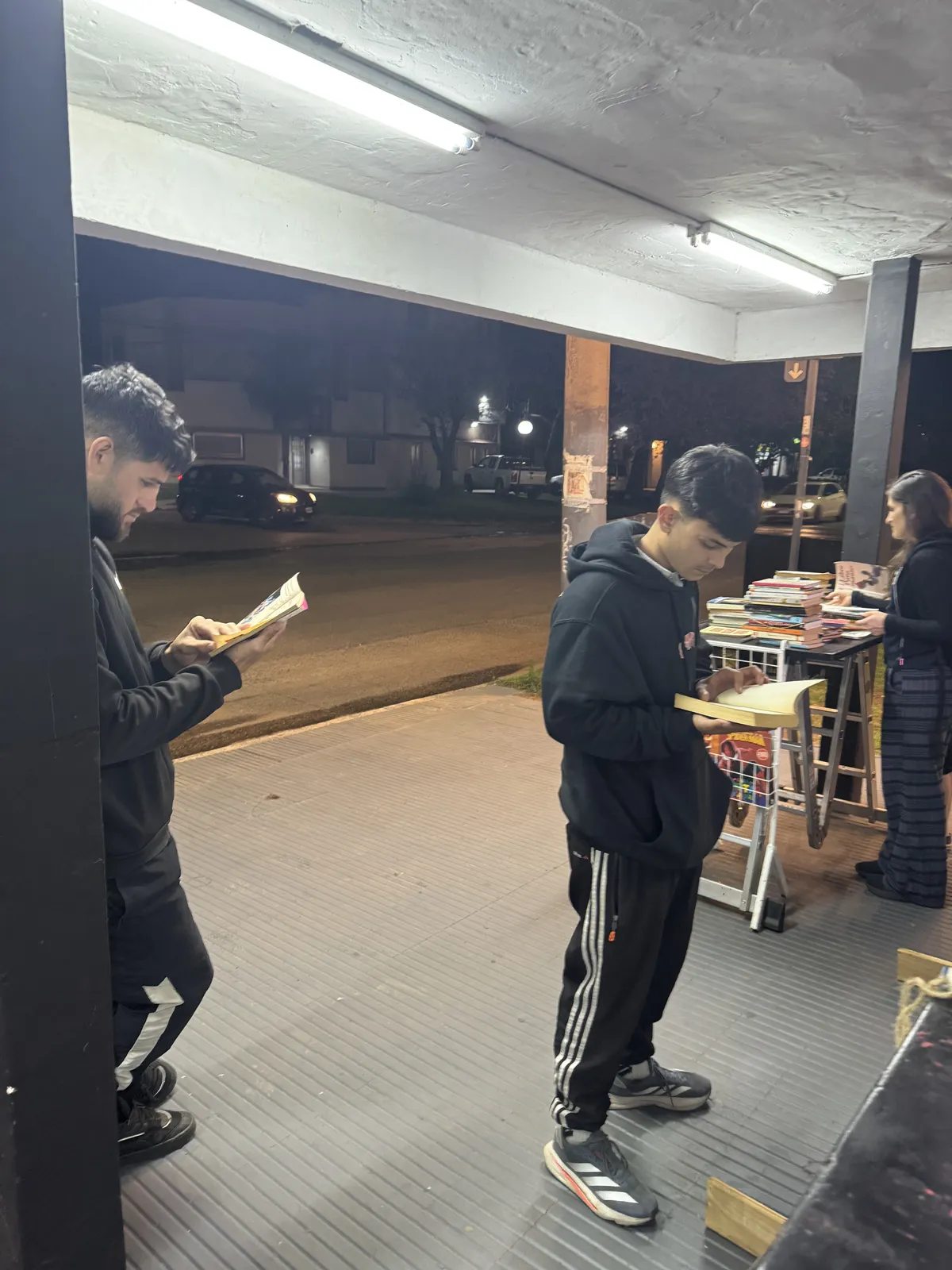 Dos jóvenes leyendo de noche en la vereda del local